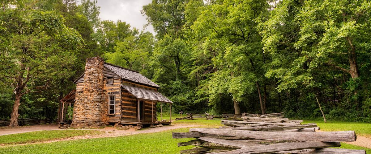 A rustic stone cabin surrounded by lush green trees and a wooden fence.