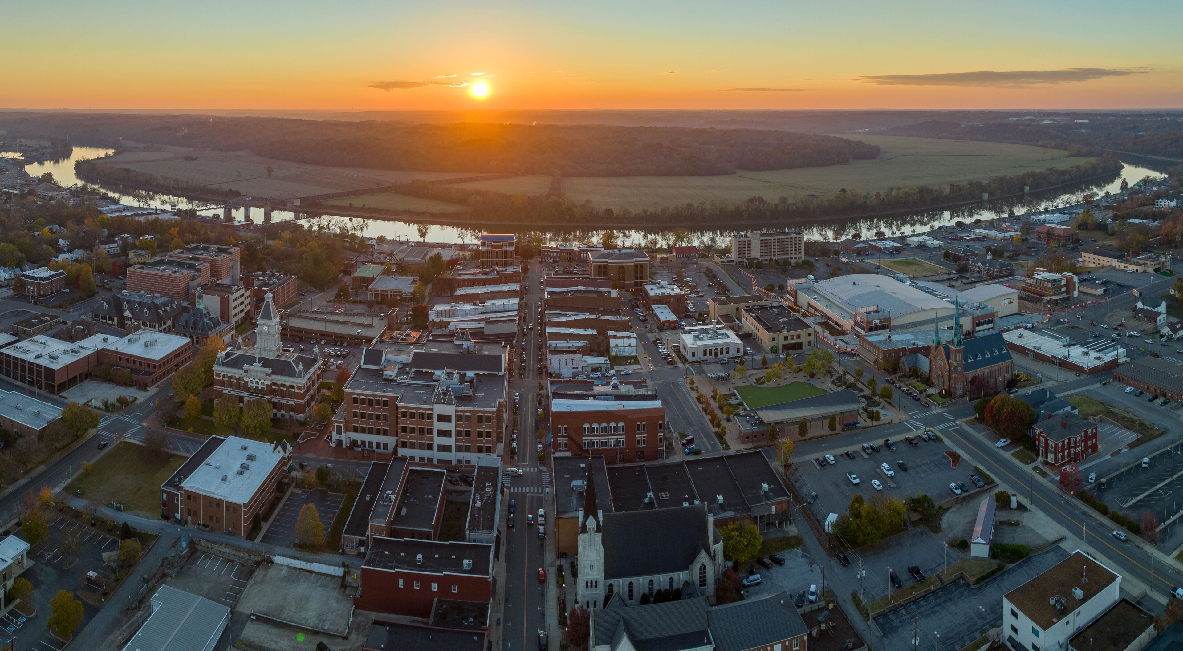 An aerial view of a town at sunset with a river and fields in the background.