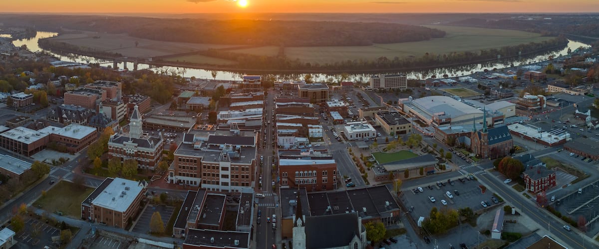 An aerial view of a town at sunset with a river and fields in the background.