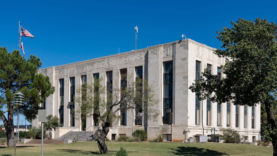 A courthouse with columns, an American flag, and a clear blue sky.