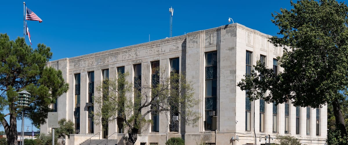 A courthouse with columns, an American flag, and a clear blue sky.