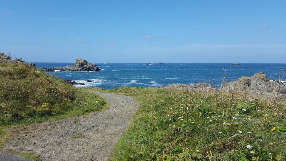 A coastal path with rocky outcrops and a lighthouse in the distance.