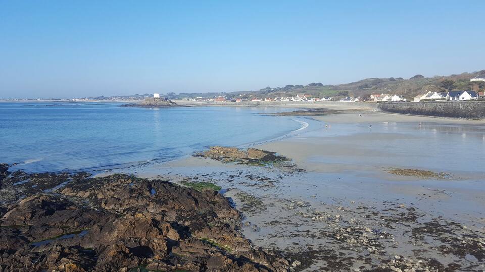 A coastal landscape with rocky shores, clear blue water, and a distant town with houses.