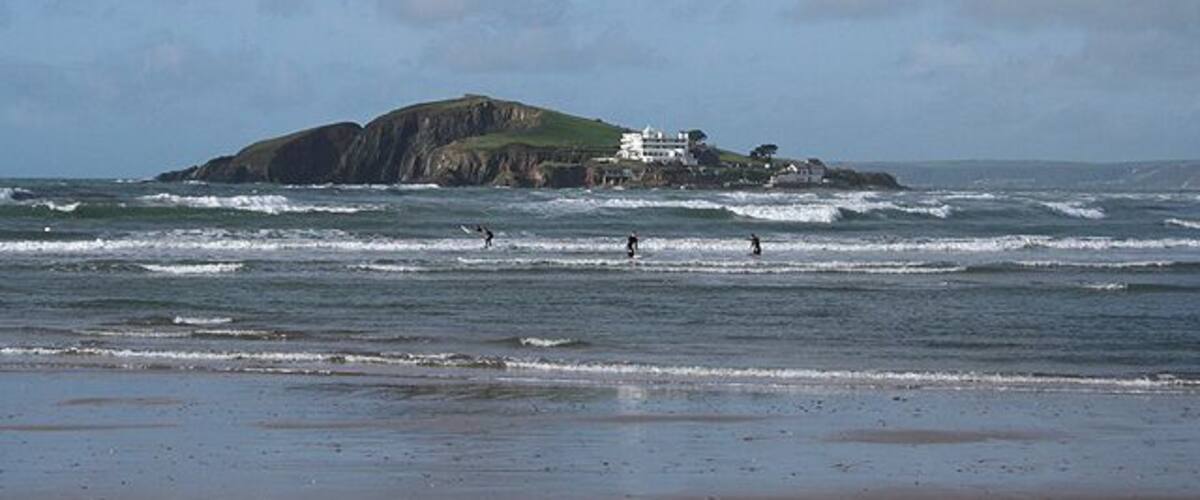 A beach with waves, a rocky island, and a white building.