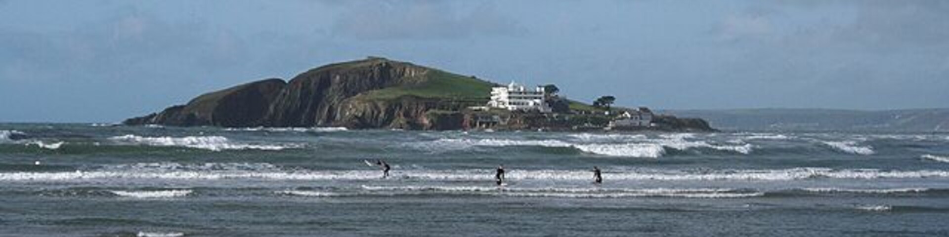 Una playa con olas, una isla rocosa y un edificio blanco.