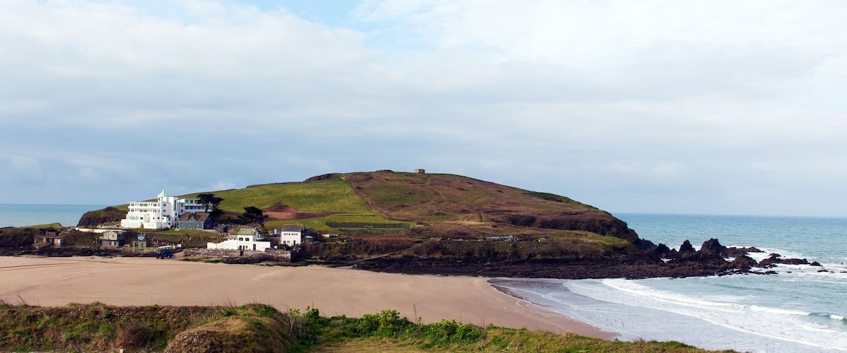 A coastal landscape with a hill, beach, and a white building complex.