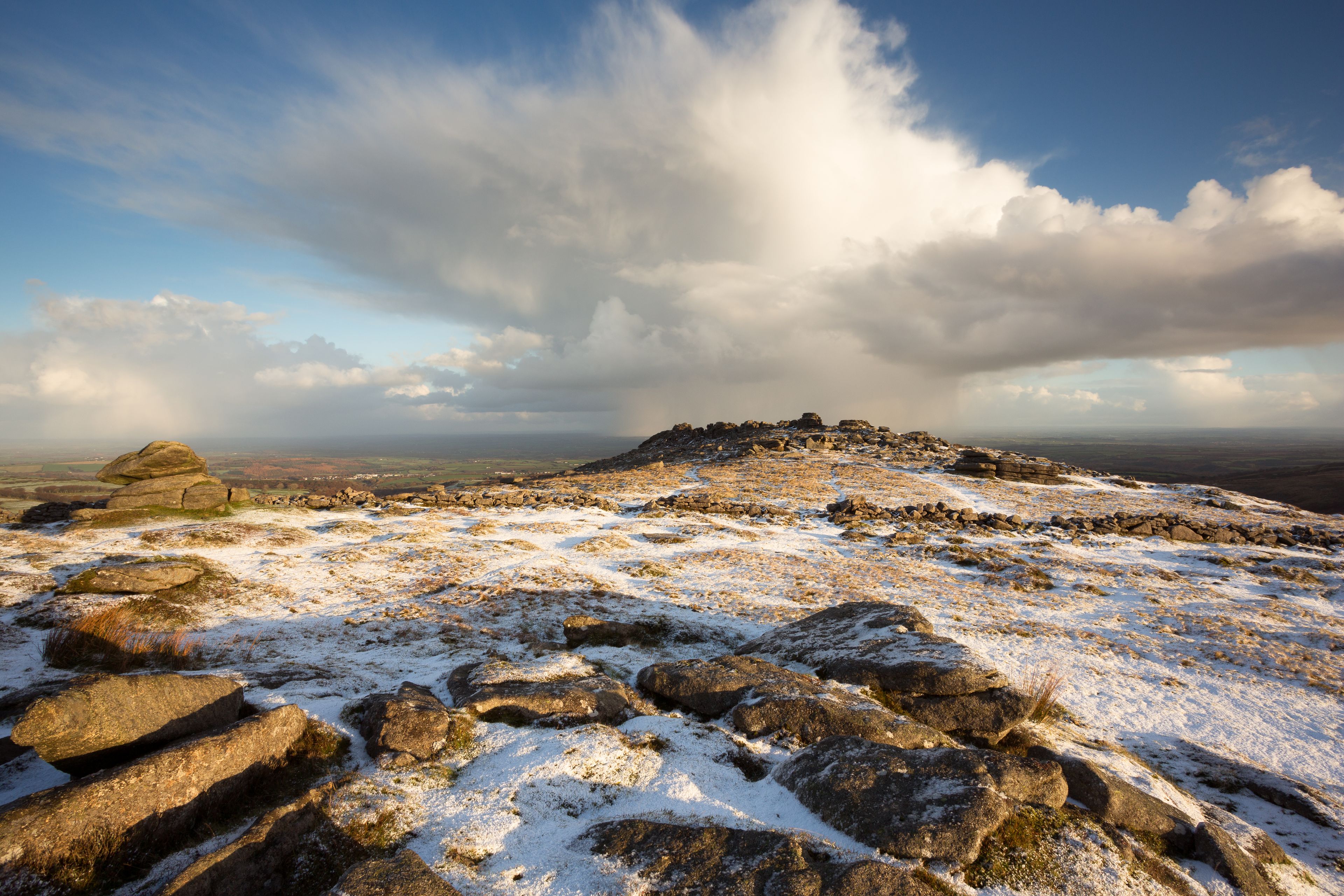 A snowy mountain landscape with rocky outcrops and a cloudy sky.