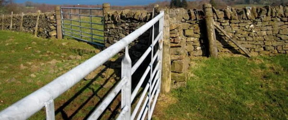 A stone wall, a metal gate, and a view of a lake with mountains in the distance.