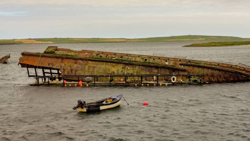 A large rusted shipwreck in a body of water with a small boat nearby.