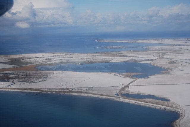 An aerial view of a coastal area with snow-covered land, water bodies, and distant clouds.