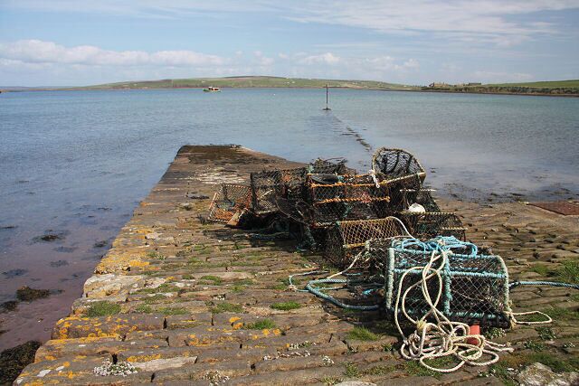 A rocky pier with lobster traps and fishing nets by a calm sea.