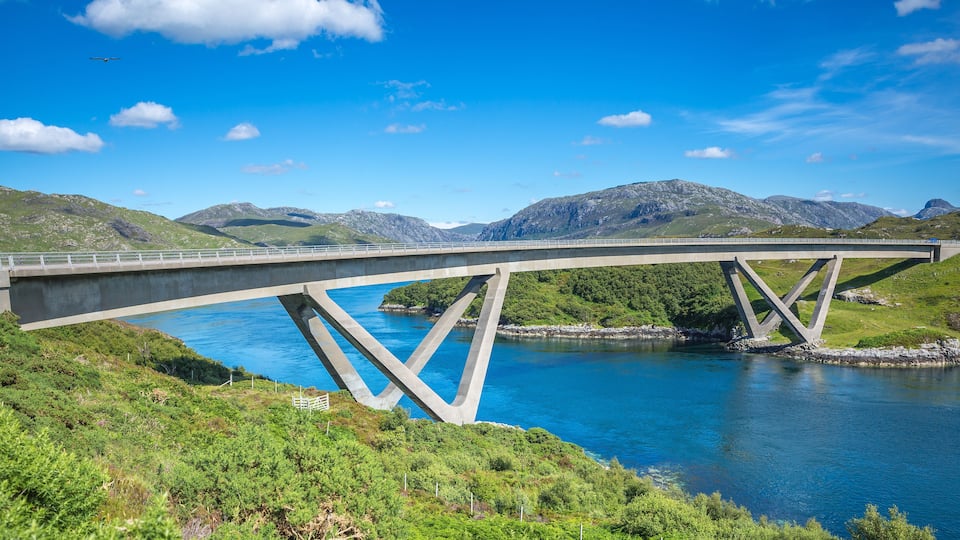 A bridge over a river with mountains in the background.
