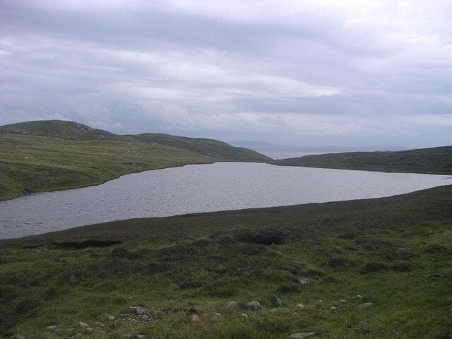 Un lago rodeado de colinas cubiertas de hierba bajo un cielo nublado.