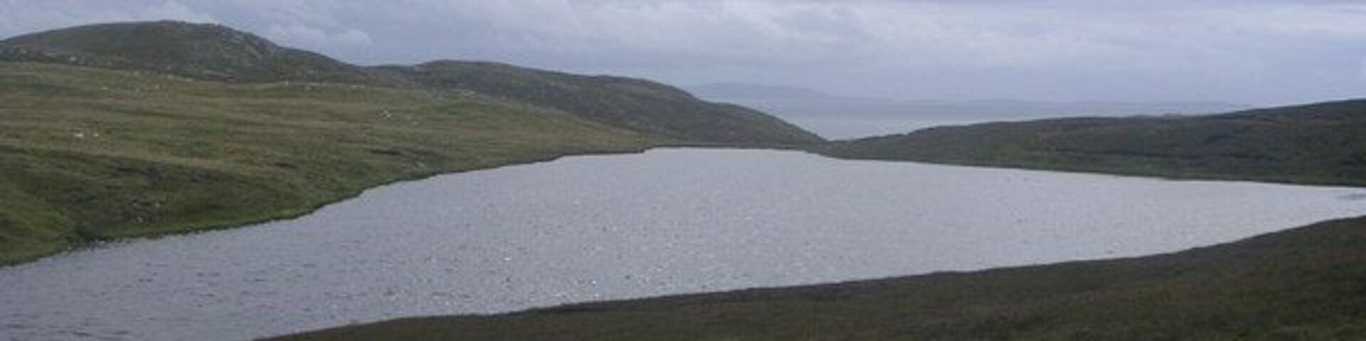 Un lago rodeado de colinas cubiertas de hierba bajo un cielo nublado.