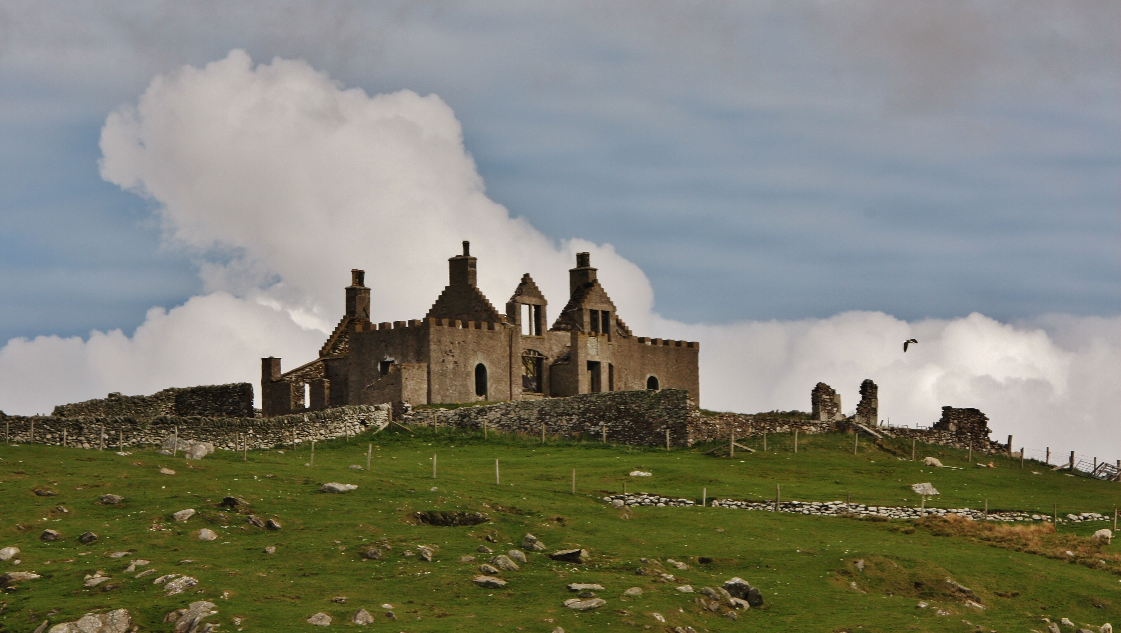 A historic castle on a grassy hill with a cloudy sky.