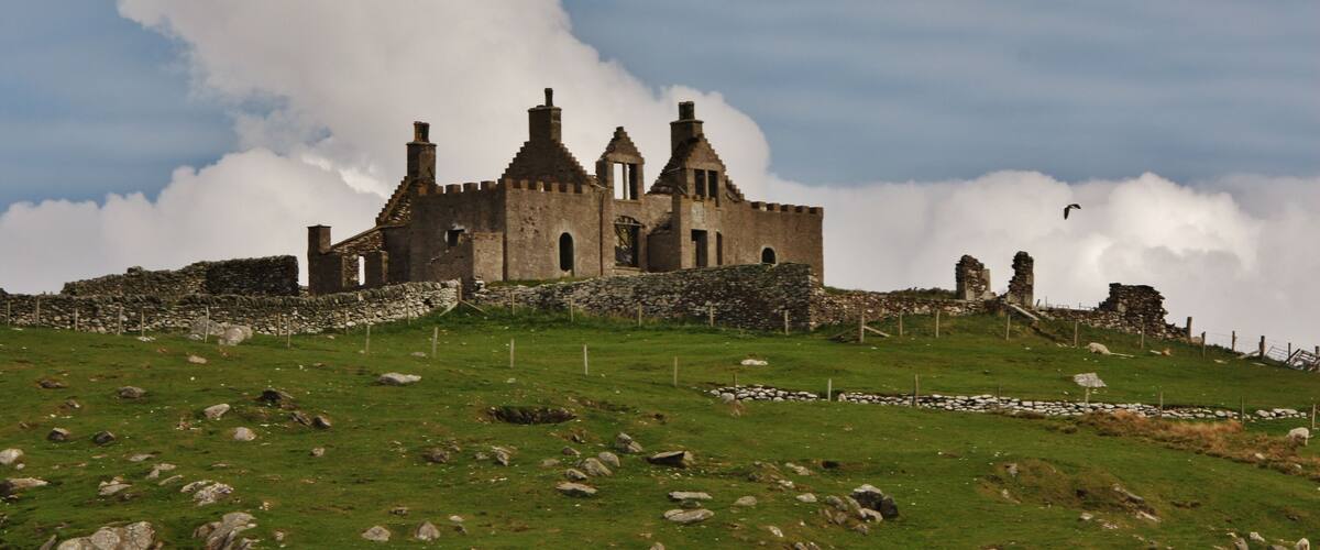 A historic castle on a grassy hill with a cloudy sky.