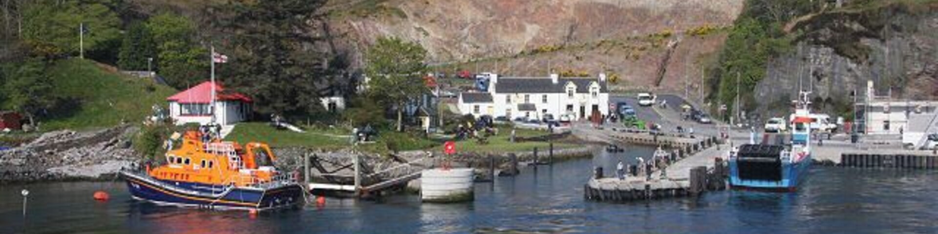 Un puerto con barcos, un edificio de techos rojos y un edificio blanco con una colina al fondo.
