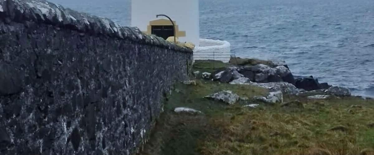 A lighthouse by the sea with a stone wall and grassy area.