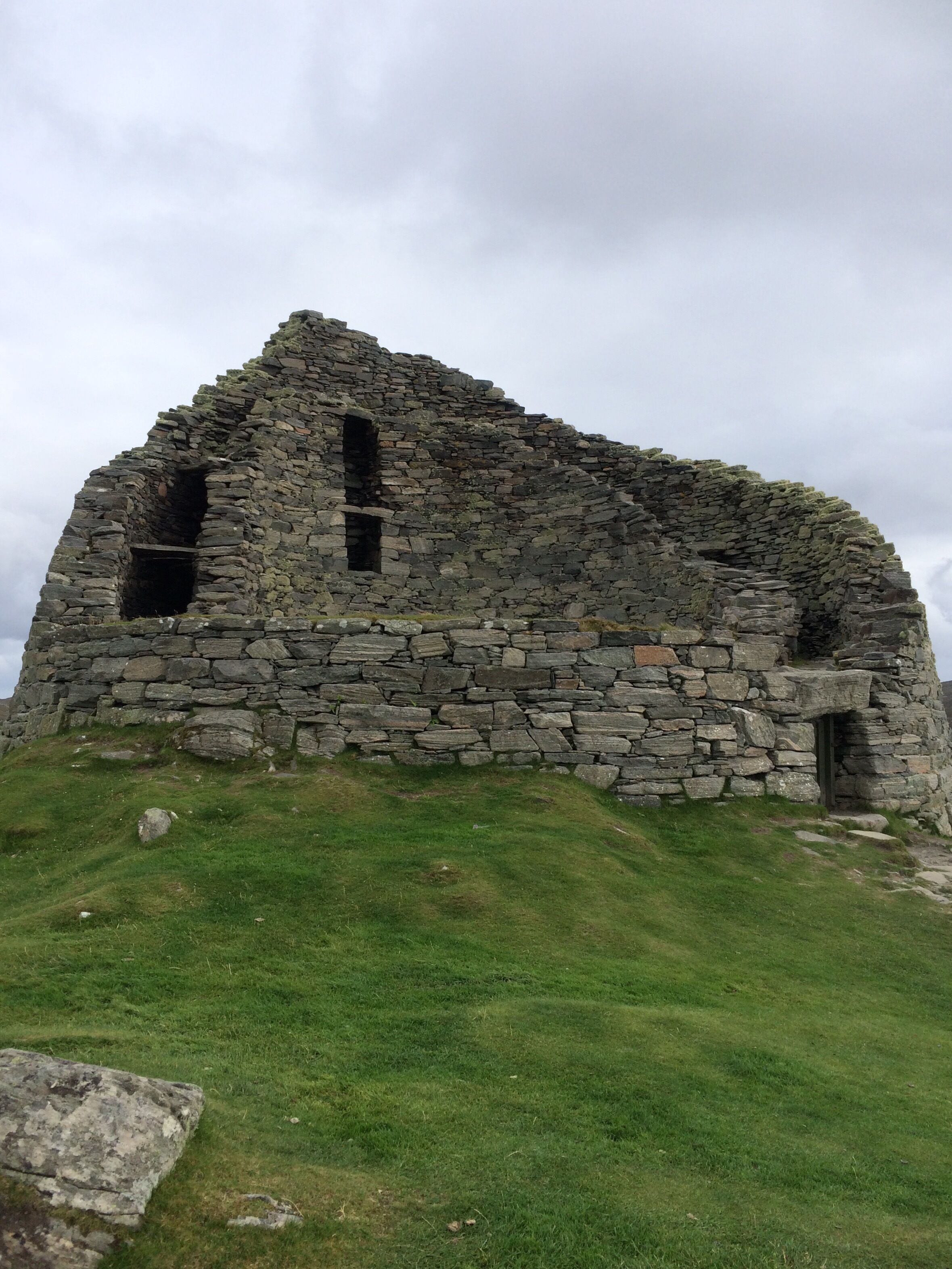 A stone ruin with two visible openings, surrounded by grassy terrain.