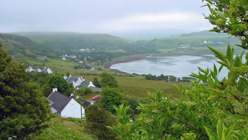 A coastal landscape with houses, a river, and rolling hills.