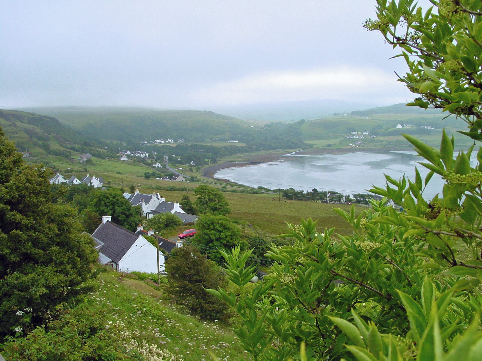 A coastal landscape with houses, a river, and rolling hills.