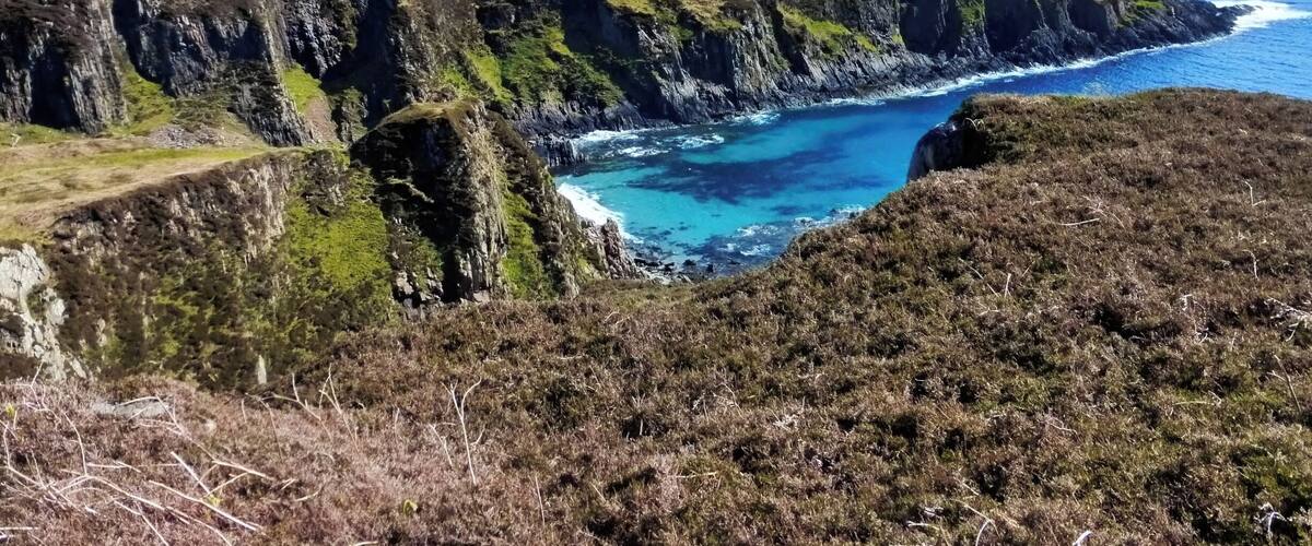 A coastal landscape with cliffs and a clear blue sea.