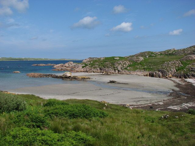 A coastal landscape with a sandy beach, rocky outcrops, and grassy hills.