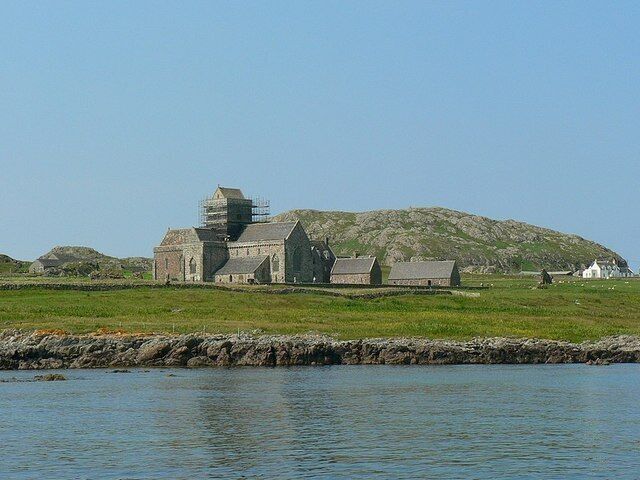 A coastal church with a stone structure, a grassy field, and a rocky shoreline.