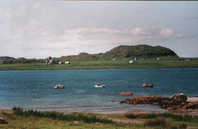 A coastal landscape with a hill, boats on the water, and scattered buildings.
