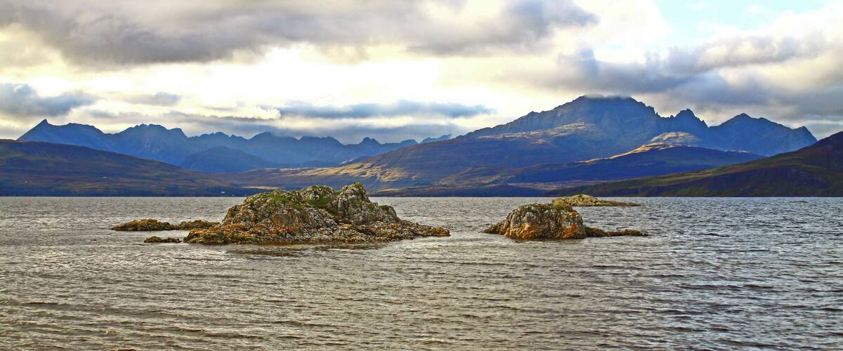A lake with rocky islands and mountains in the background.