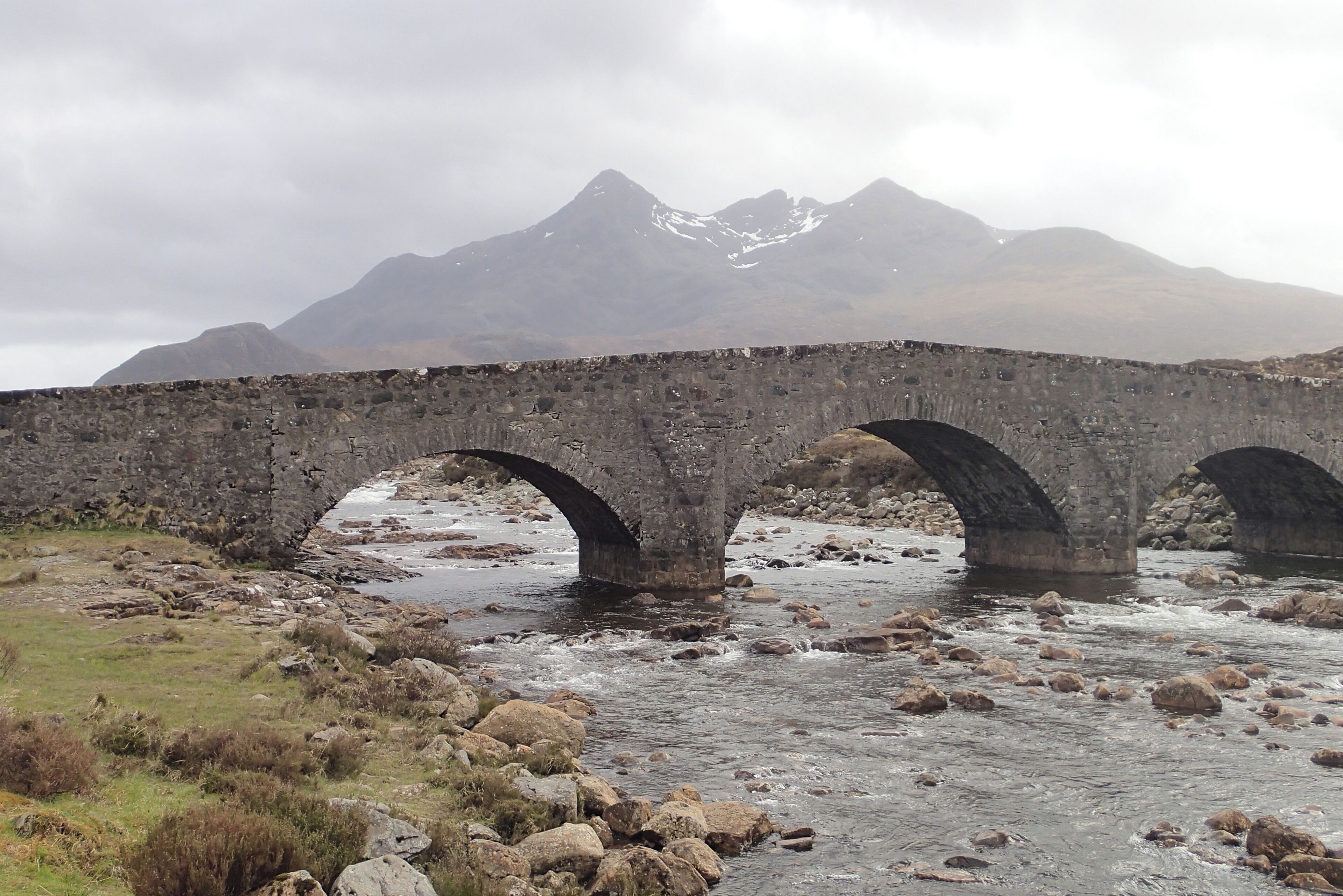 A stone bridge over a river with mountains in the background.
