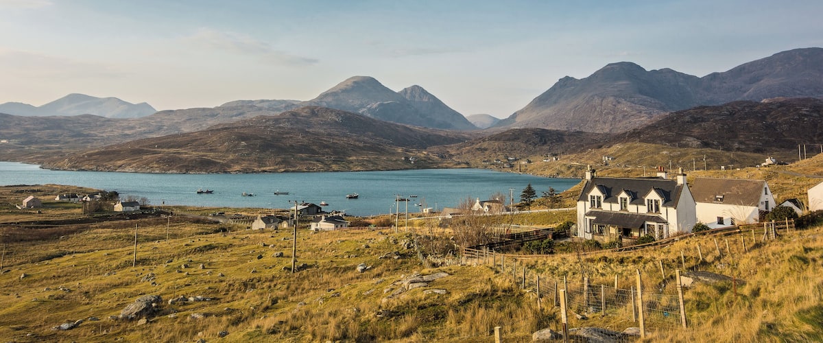A coastal village with houses, a church, and mountains in the background.