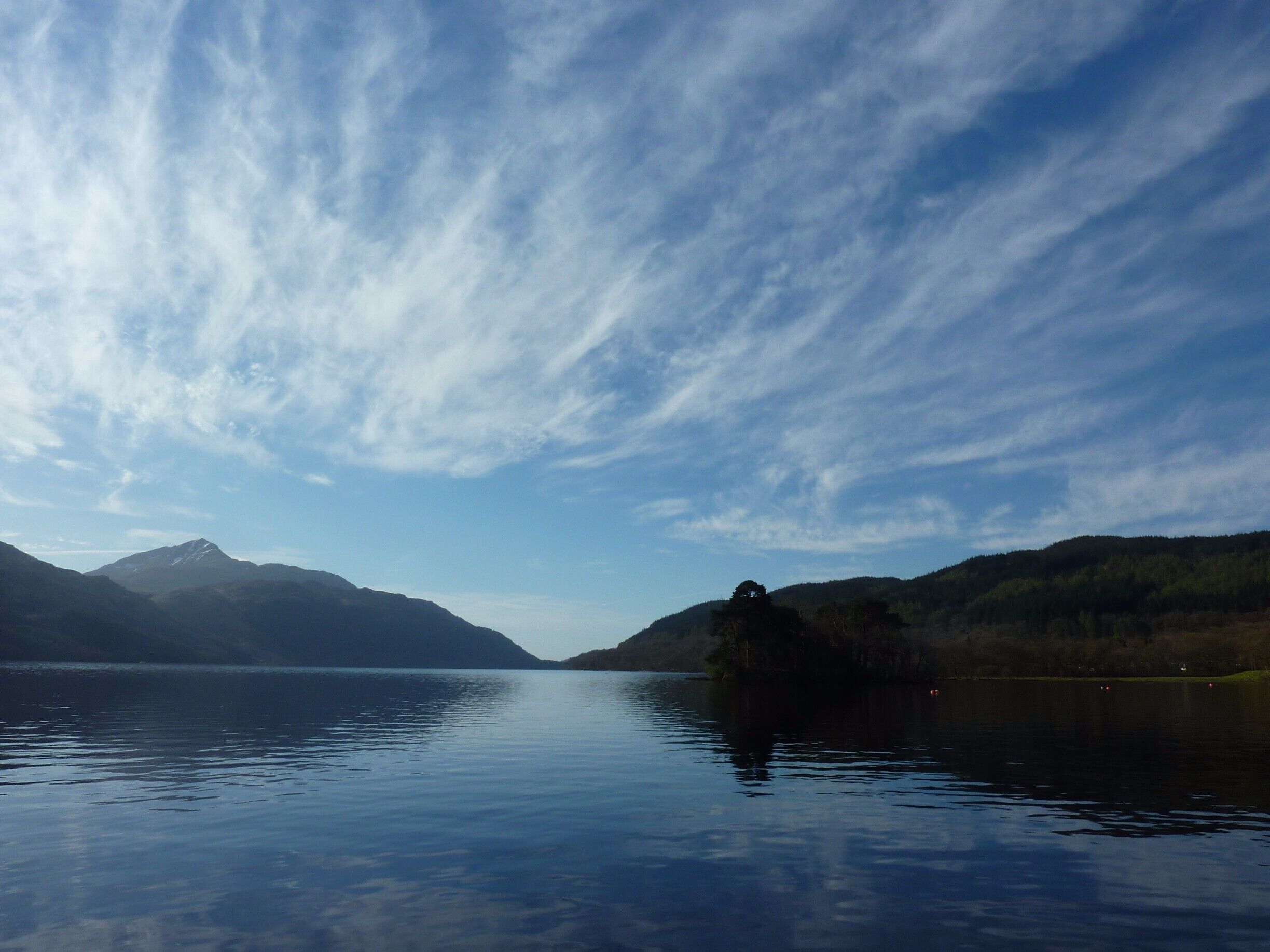 A calm lake with mountains in the background and a clear sky.