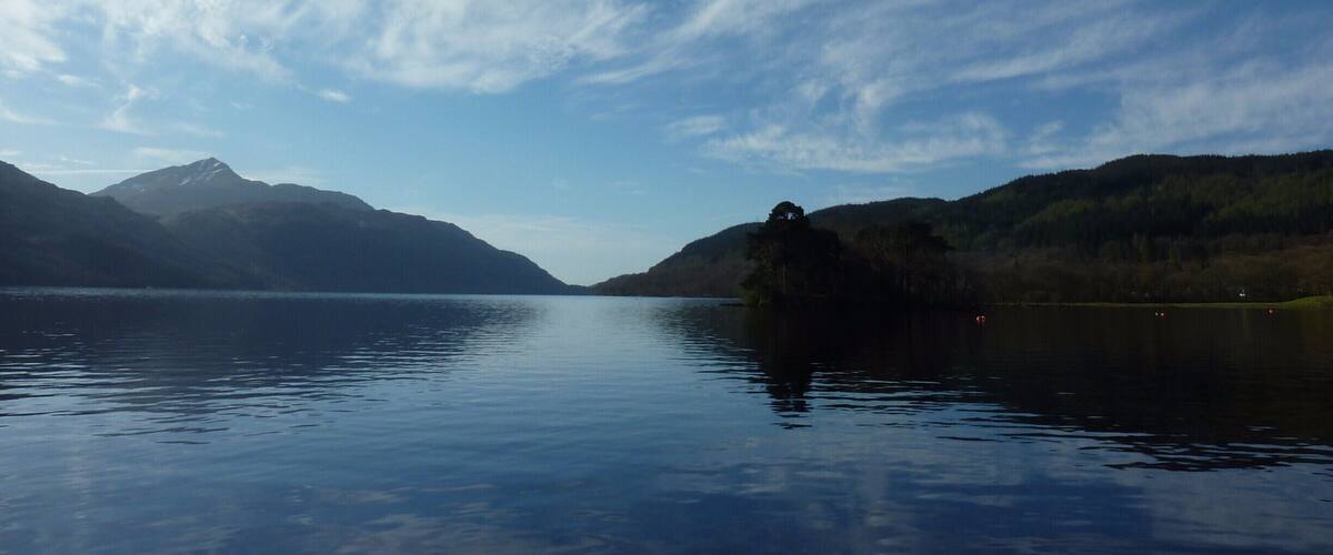 A calm lake with mountains in the background and a clear sky.