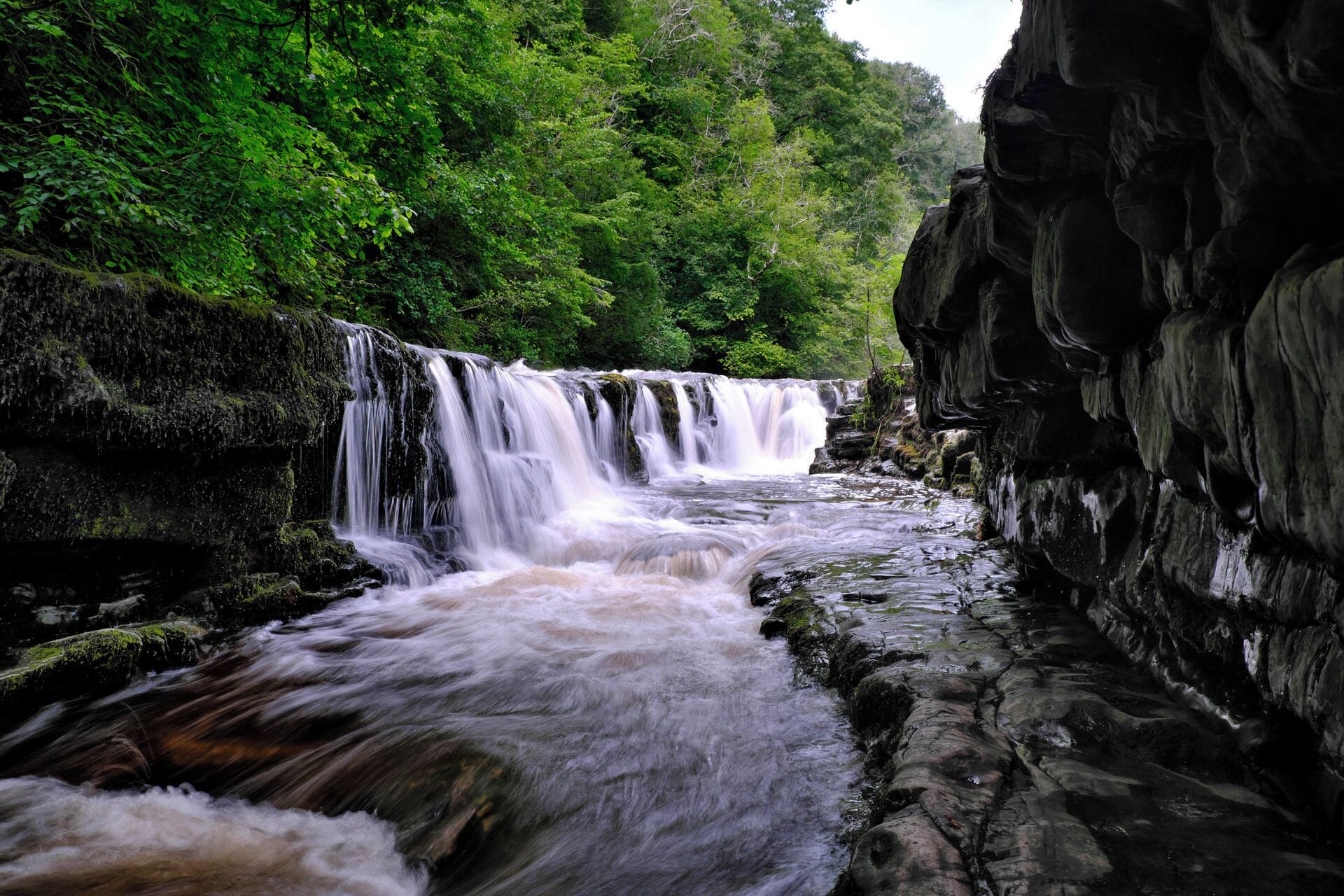 A waterfall cascading over rocky terrain surrounded by dense green foliage.