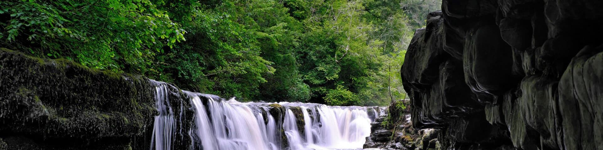 A waterfall cascading over rocky terrain surrounded by dense green foliage.