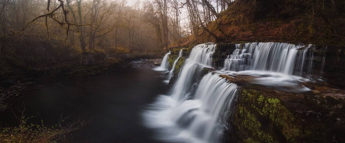 A waterfall cascading over moss-covered rocks in a forested area.