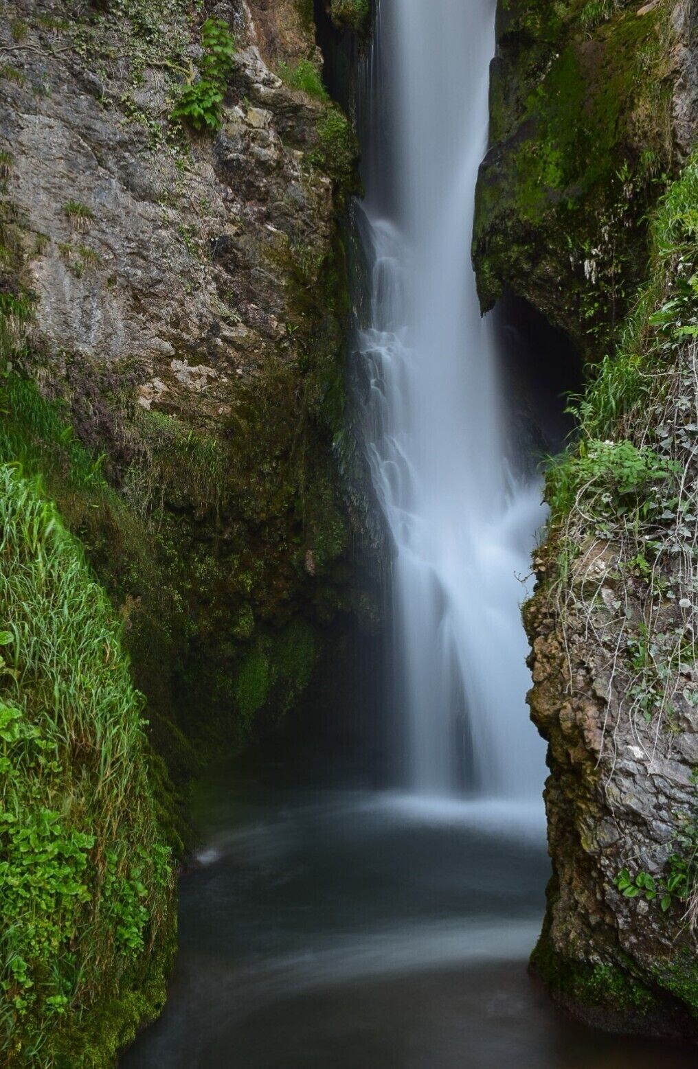 A waterfall cascading through a rocky gorge with lush green vegetation on the sides.