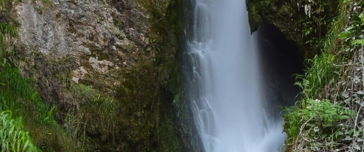 A waterfall cascading through a rocky gorge with lush green vegetation on the sides.