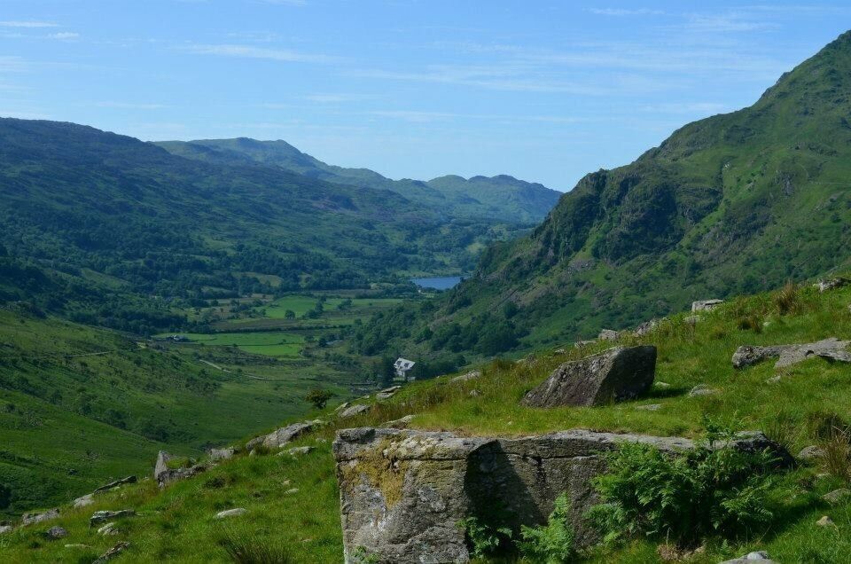 A valley with a lake, green hills, and a stone structure.
