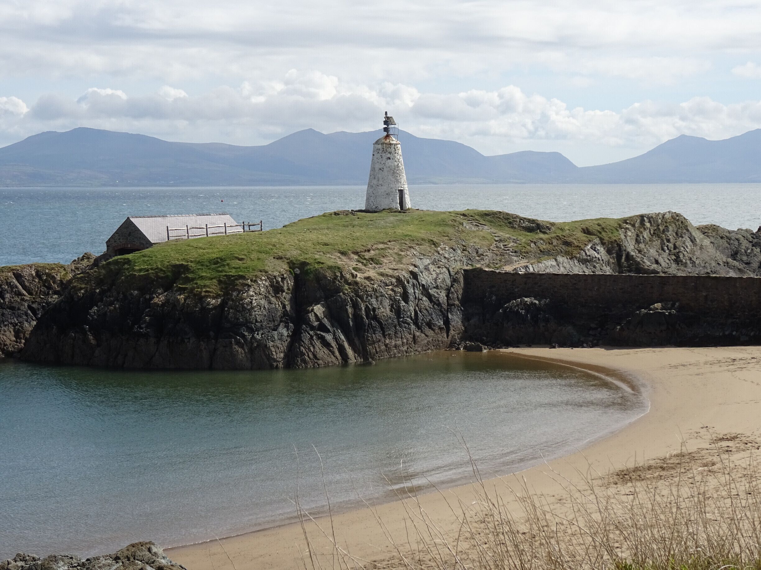 A lighthouse on a grassy cliff by the sea, with mountains in the background.