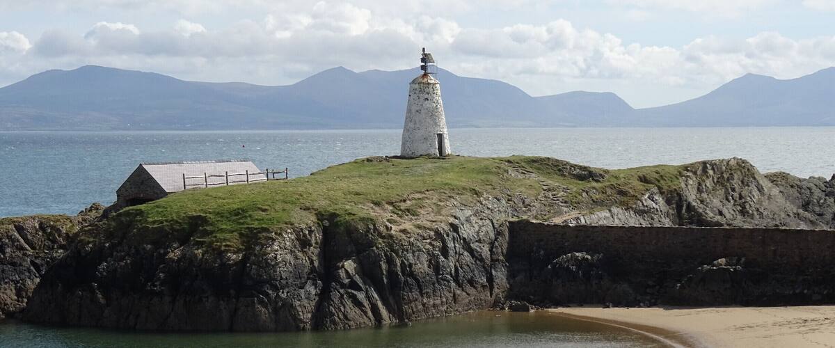 A lighthouse on a grassy cliff by the sea, with mountains in the background.