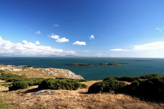 A coastal landscape with rocky terrain, green vegetation, and a clear blue sky.