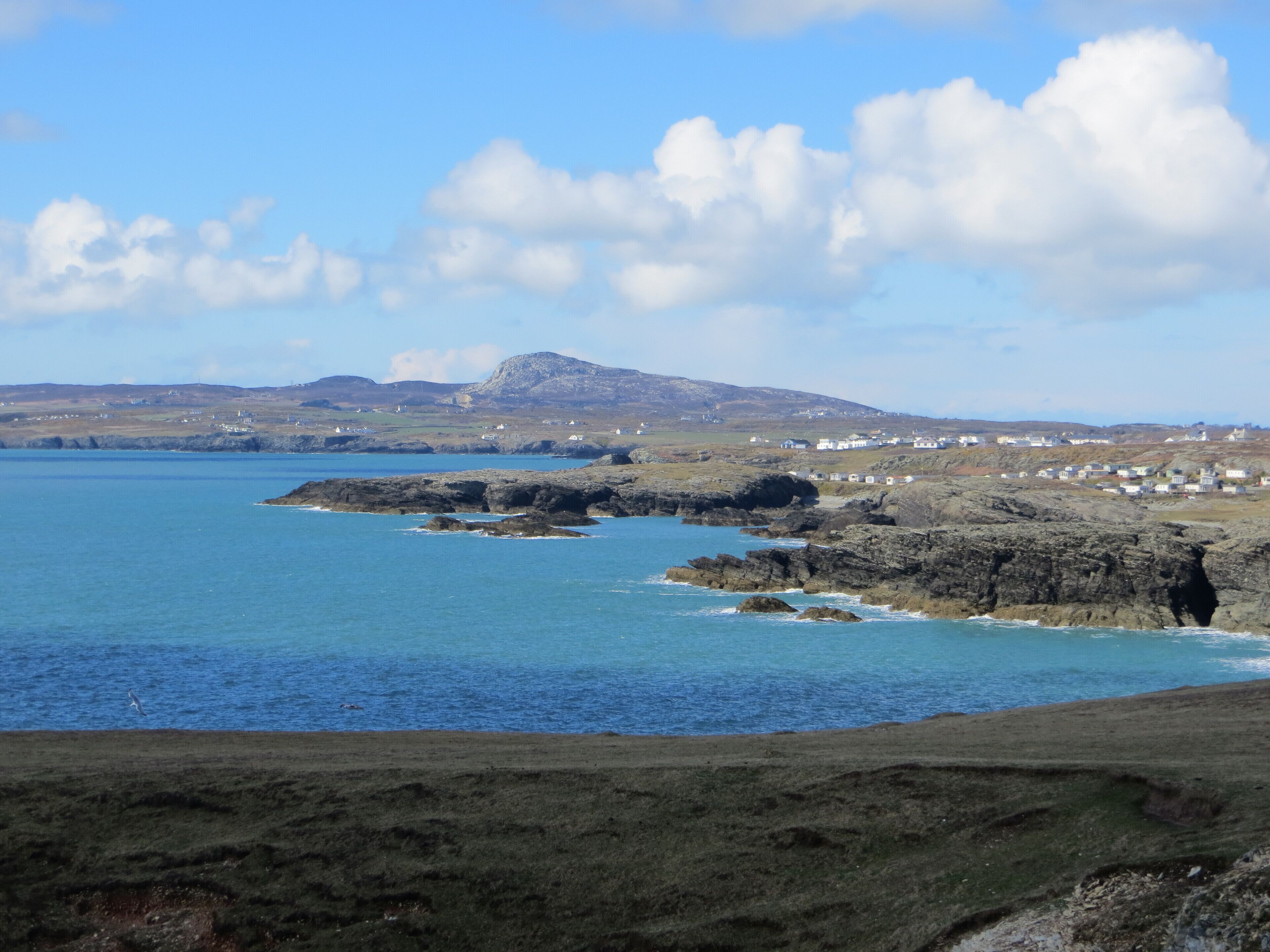 A coastal landscape with rocky shores, a clear blue sea, and a distant mountain.