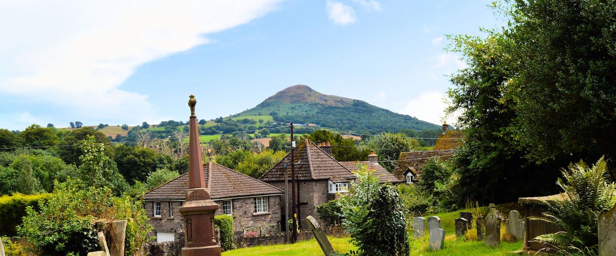 A rural cemetery with stone headstones, a stone church, and a hill in the background.
