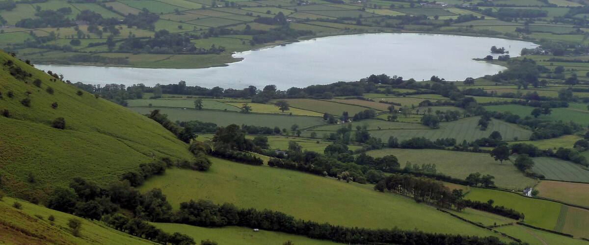 Un lago rodeado de colinas verdes ondulantes y montañas a lo lejos.