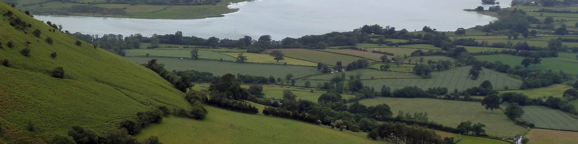 A lake surrounded by rolling green hills and distant mountains.