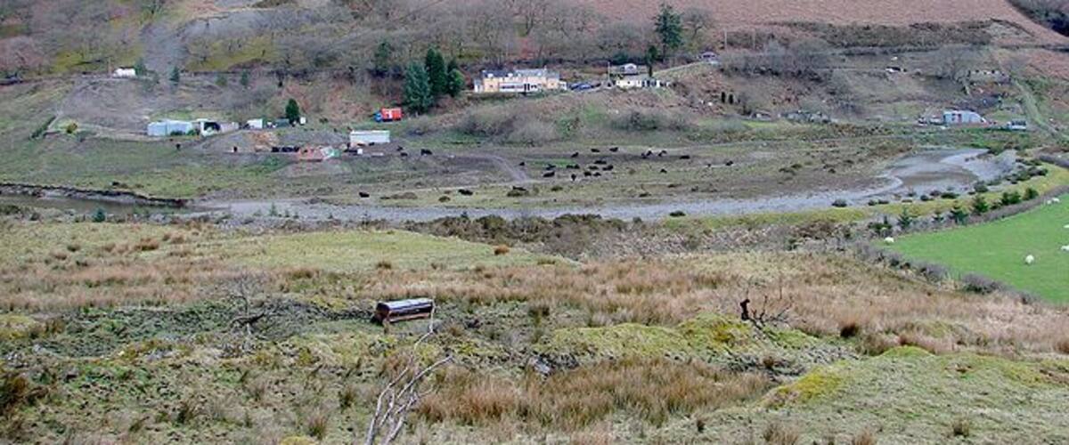 A rural landscape with a hill, a small village, and a stream.