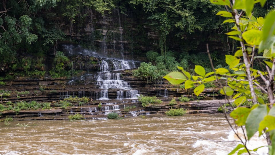 A multi-tiered waterfall cascading over rocky terrain surrounded by dense greenery.