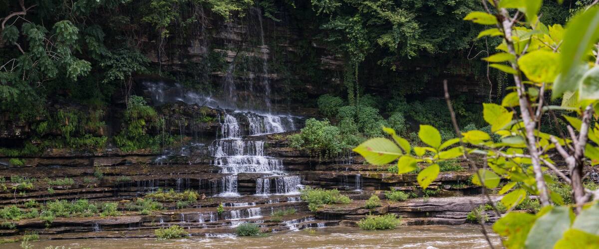 A multi-tiered waterfall cascading over rocky terrain surrounded by dense greenery.